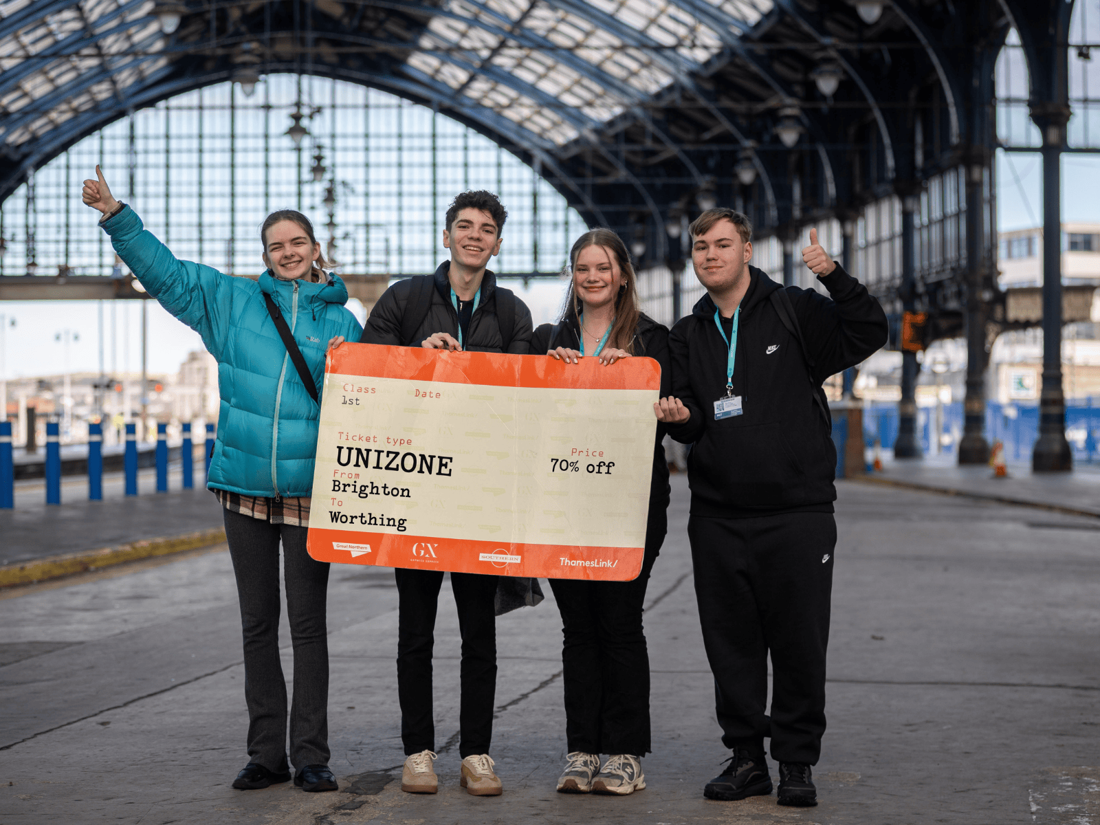 Four students stood in a railway station, holding a big train ticket